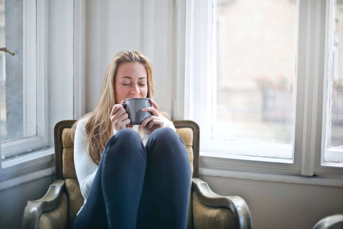 Picture of a woman sipping tea on a sofa.