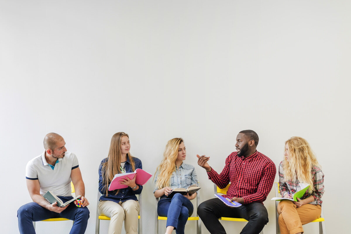 Picture of students sitting in front of a wall, some talking.