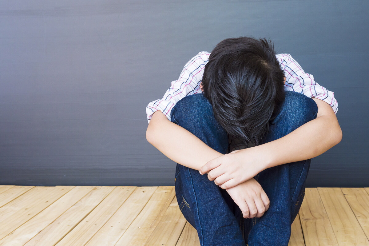 Picture of a sad boy sitting at a wall.